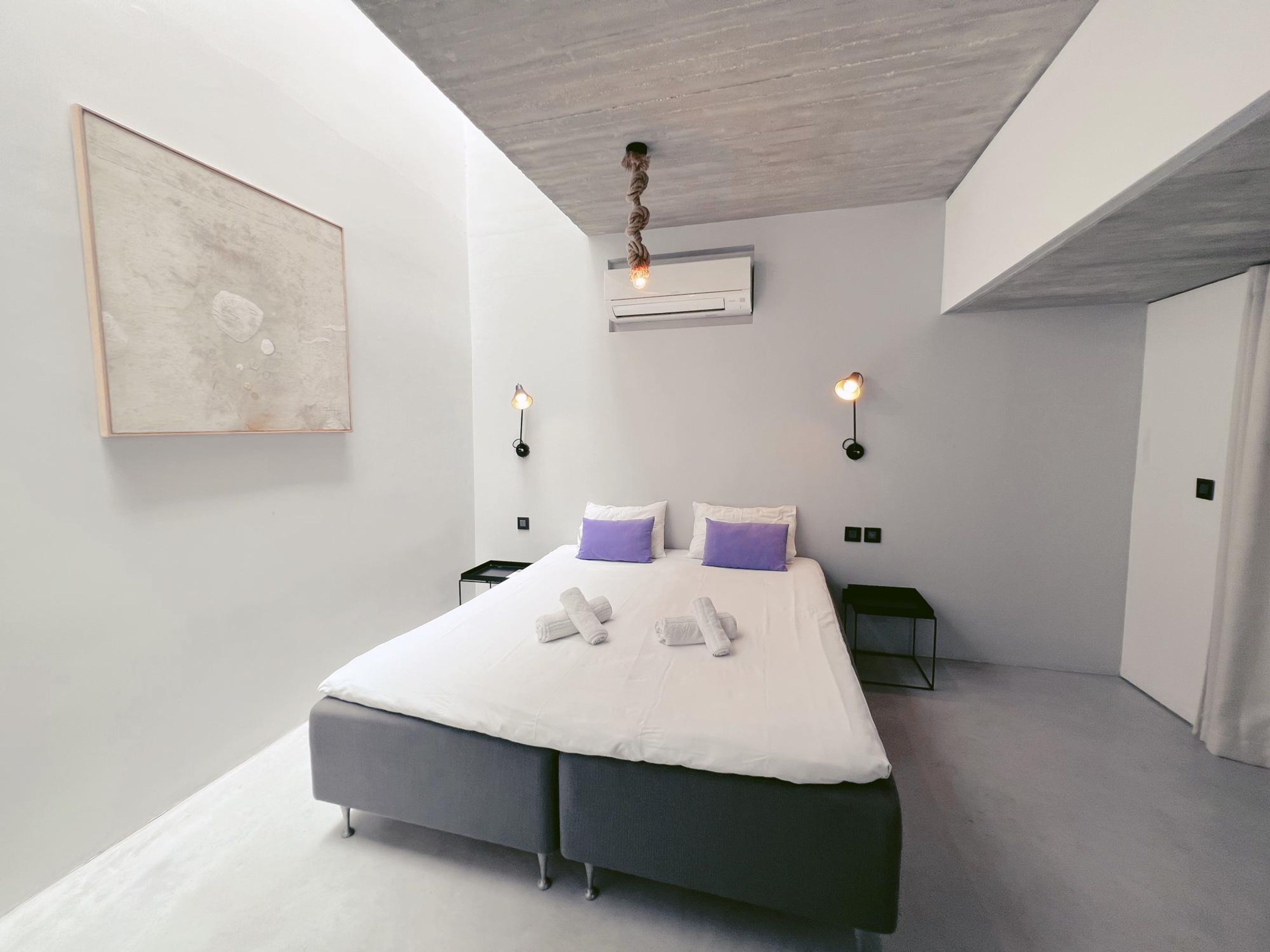 Et moderne soveværelse med en stor seng, to sengeborde, en vægmonteret aircondition og en usædvanlig loftlampe.