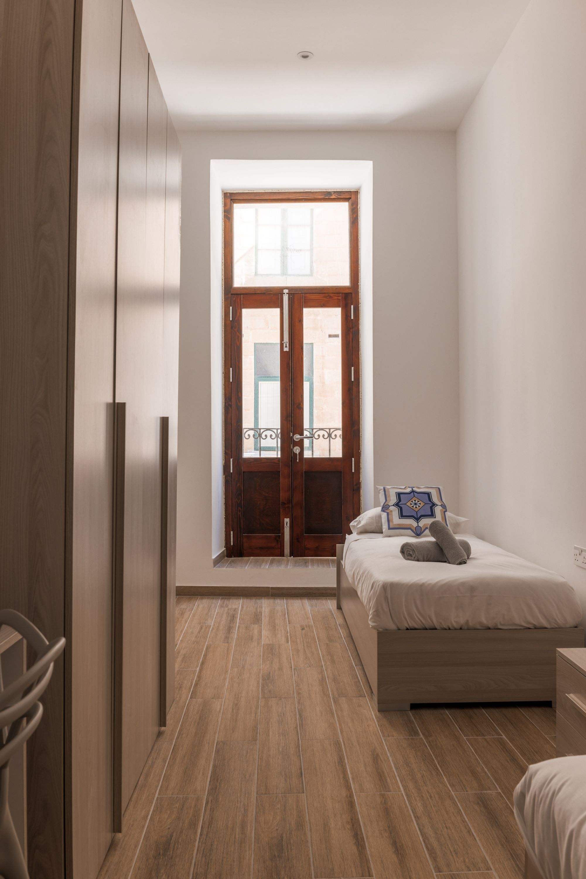 A bedroom with a wooden wardrobe, a bed with a pillow, and a window with a view of the outside.