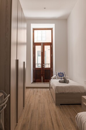 A bedroom with a wooden wardrobe, a bed with a pillow, and a window with a view of the outside. - 2BR in Historic Valletta Prime Central Location (Valletta)