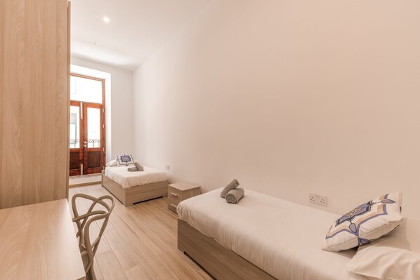 A minimalist bedroom with a wooden floor, a bed with a pillow, a bedside table, and a chair.