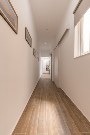 A hallway with wooden flooring, framed pictures on the walls, and a window on the right.