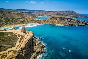 A coastal landscape with a rocky cliff, a small tower, and a beach.