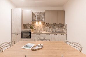 A modern kitchen with light wood cabinets, a built-in oven, and a patterned backsplash.
