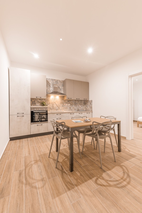 A modern kitchen with a dining area, featuring a wooden table and chairs, a built-in oven, and a tiled backsplash.