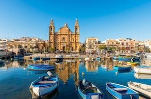 A harbor with boats, a prominent church with two towers, and surrounding buildings.