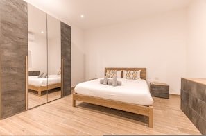 Une chambre à coucher moderne avec un lit en bois, un grand miroir et une petite table de chevet.