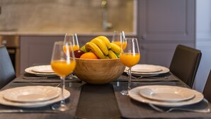 A dining table set with plates, a wooden bowl of fruit, and glasses of orange juice. - Square and Sea Views - 1 BR With Ensuite (Valletta)