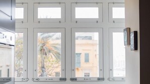A room with a view through a window, a chair, a small table with a plate and glasses, and a wall-mounted picture. - Square and Sea Views - 1 BR With Ensuite (Valletta)