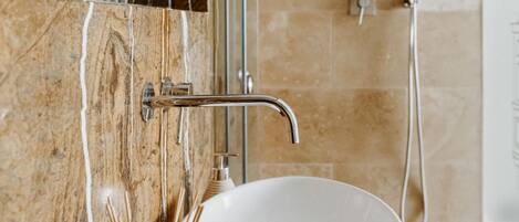 A bathroom with a marble sink, a glass vase with reed sticks, and a shower area.
