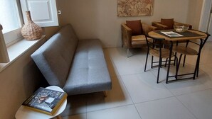 Una sala de estar con un sofá gris, una mesita redonda con un libro, una mesa de comedor de madera con sillas y un cuadro grande en la pared.