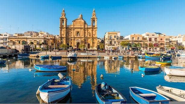 Un puerto con barcos amarrados frente a un edificio histórico con dos torres.