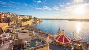 A coastal cityscape with a prominent fortress-like structure, a domed building, and a harbor area with boats and docks. - Luxury Penthouse With a Terrace (Sliema)