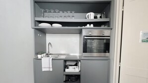 Cocina compacta con lavamanos, horno y estantes para vajilla y copas.