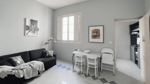 Un espacio habitable compacto con sofá, una mesa de comedor con sillas, una pequeña cocina y obras de arte en las paredes.