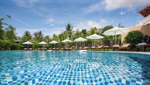 A swimming pool with clear blue water, surrounded by lounge chairs and umbrellas, set against a backdrop of lush greenery and a clear sky. - Herbal Resort (Phu Quoc)
