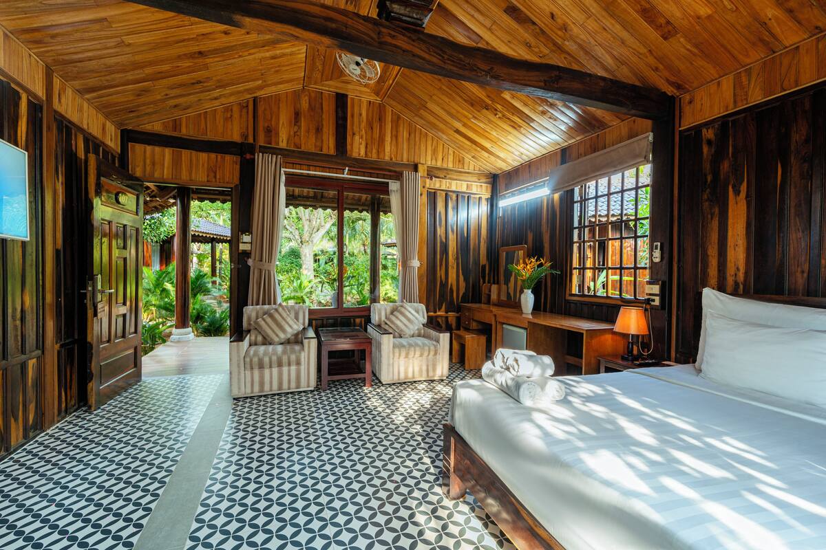 Une pièce spacieuse avec un grand lit, un plafond en bois et une vue sur une végétation luxuriante.