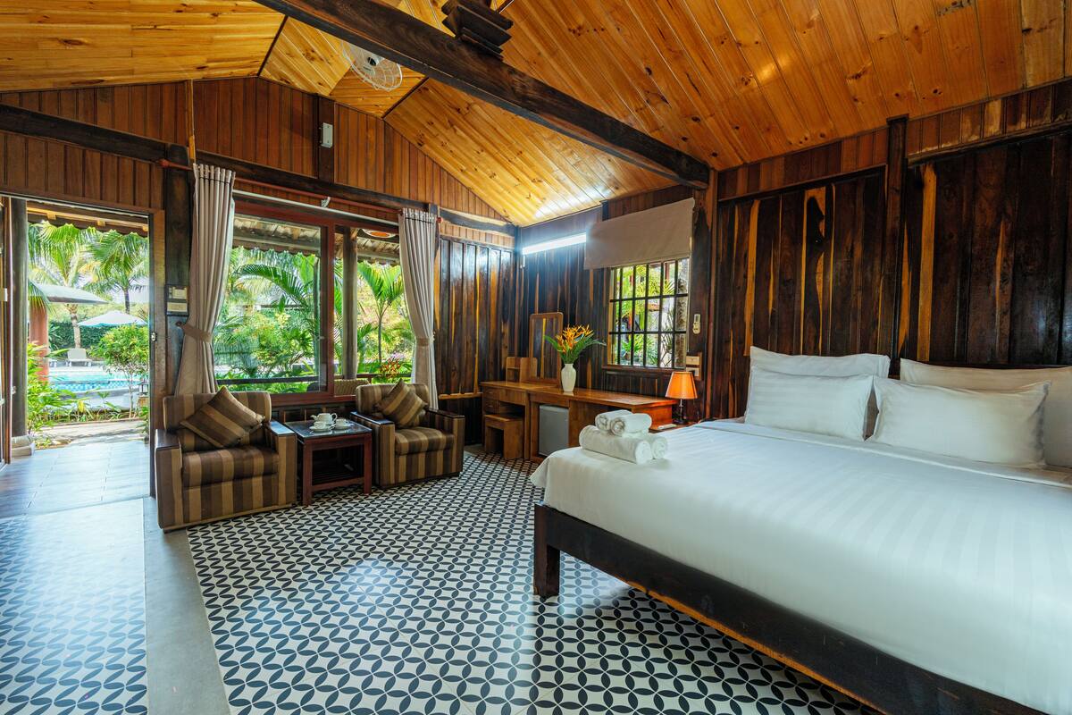 Une chambre dotée d’un grand lit, d’un canapé, d’un bureau et offrant une vue sur la verdure environnante.