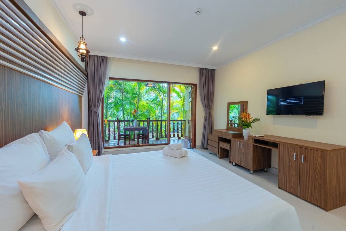 Une chambre d’hôtel avec un grand lit, un bureau, une télévision et un balcon donnant sur un paysage verdoyant.