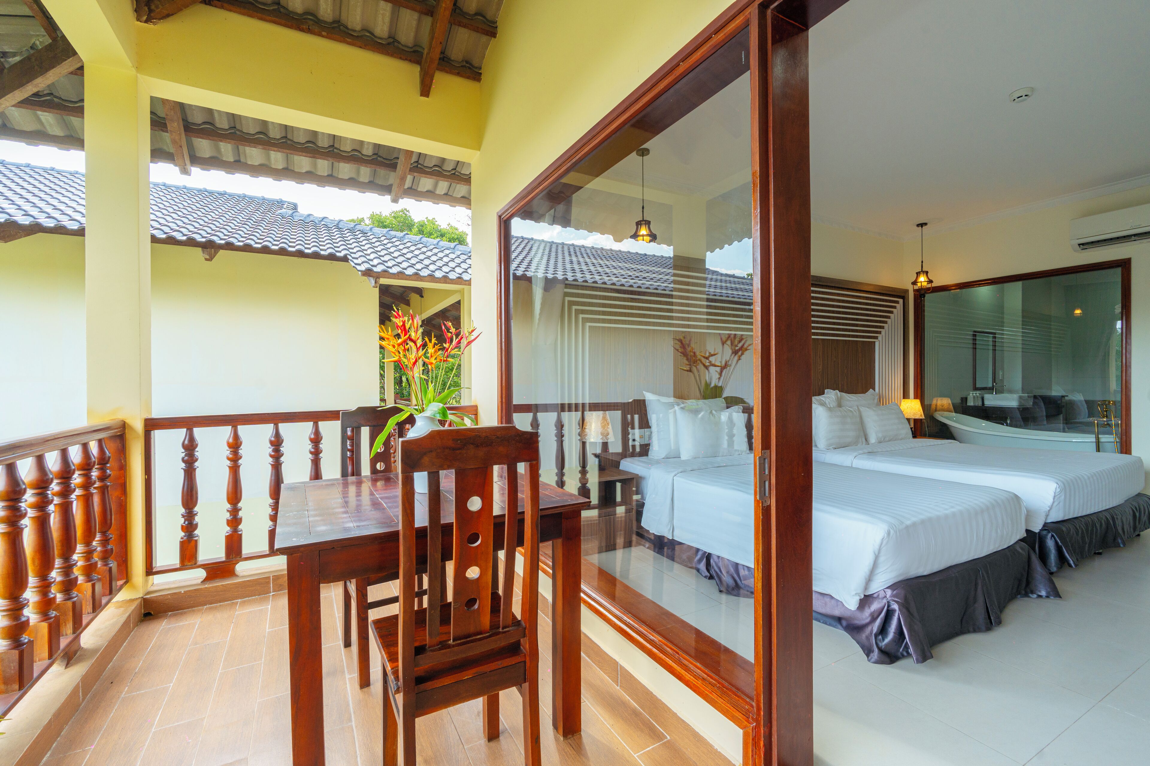 Quarto de hotel com varanda, mesa de jantar e cama com duas almofadas.