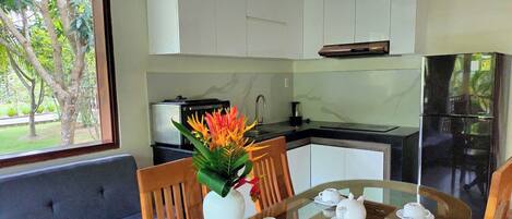 A modern kitchen with white cabinets, a black refrigerator, and a dining area with a glass table and chairs.
