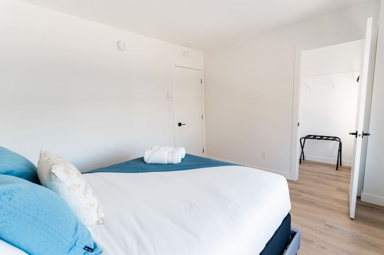 Une chambre à coucher avec un lit, des oreillers, une serviette pliée et une porte donnant sur une autre pièce.