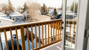 En balkong med ett träräcke, en skjutdörr i glas och utsikt över ett bostadsområde med hus och träd.