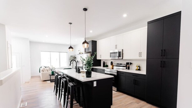 Une cuisine moderne dotée d’un îlot central, de meubles de couleur noire et de luminaires suspendus.