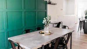 Un espace repas avec une longue table, des chaises noires, un mur d’accent vert et un luminaire suspendu.