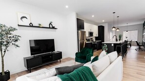Un salon moderne doté d’un téléviseur à écran plat, d’un canapé, d’un fauteuil vert et d’un coin repas avec une table et des chaises.