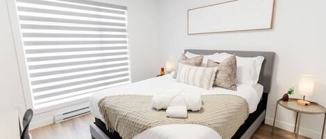 Une chambre bien rangée, avec un lit, des tables de chevet et une fenêtre équipée de stores.