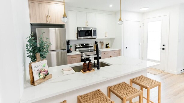 A modern kitchen with white cabinetry, stainless steel appliances, and a marble island. - *Refresh | Central & Trendy | 5 min to downtown* (Winnipeg)