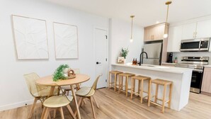 A modern kitchen with white cabinetry, stainless steel appliances, and a central island with stools. - *Refresh | Central & Trendy | 5 min to downtown* (Winnipeg)