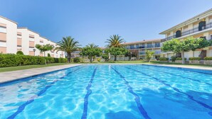 A swimming pool with clear blue water, surrounded by buildings with balconies and palm trees. - Costa Brava X-3 in Calella de Palafrugell (Palafrugell)