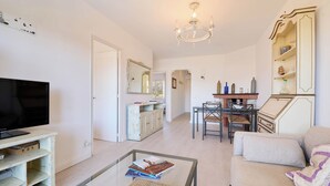 A living room with a television, a glass coffee table, a sofa, a dining table with chairs, and a chandelier. - Costa Brava X-3 in Calella de Palafrugell (Palafrugell)
