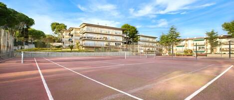 An outdoor tennis court with a net, surrounded by buildings and trees.