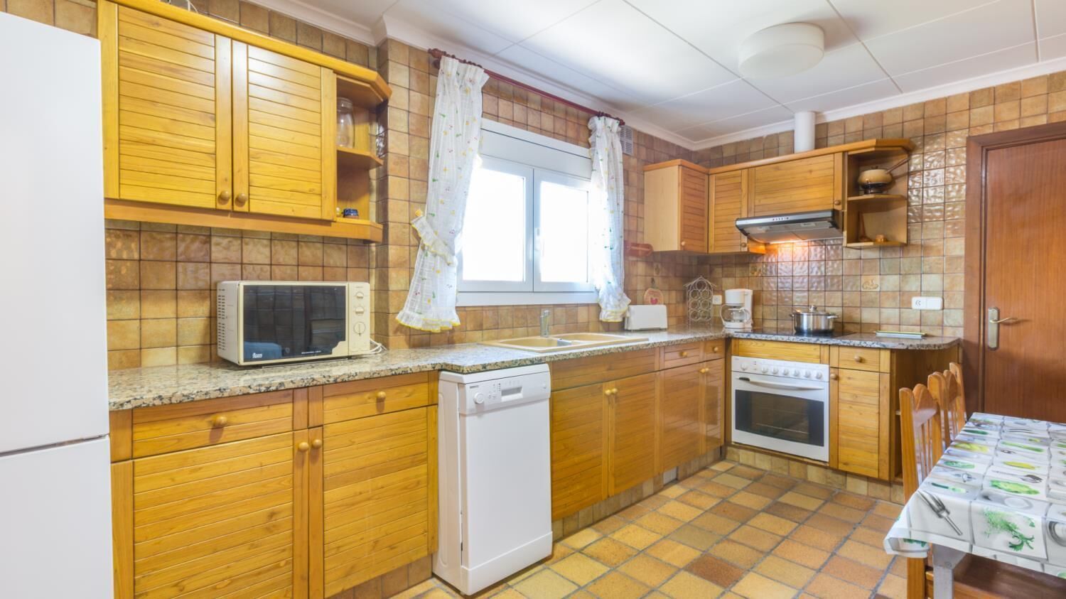 Eine kleine Küche mit Holzausstattung, einem Geschirrspüler, einer Mikrowelle, einem Spülbecken und einem Backofen.
