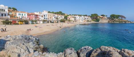 A coastal town with a sandy beach, rocky shoreline, and colorful buildings along the sea.