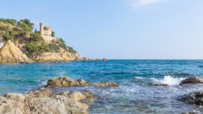 Un paysage côtier avec un château perché sur une falaise rocheuse, dominant la mer.
