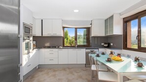 Une cuisine moderne avec des meubles blancs, un réfrigérateur en acier inoxydable, un four encastré et une fenêtre donnant sur un paysage verdoyant.
