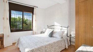 Une chambre à coucher avec un lit, une fenêtre donnant sur un paysage verdoyant, une table de chevet avec une lampe et une armoire en bois.