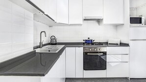 A modern kitchen with white cabinetry, a black countertop, a gas stove, a microwave, and a kettle. - Ancora 13 B-P in Llafranc (Palafrugell)