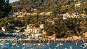 A coastal town with buildings on a hillside, a marina with boats, and a rocky breakwater. - Ancora 13 B-P in Llafranc (Palafrugell)