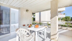 Varanda com mesa posta para dois, cadeiras brancas e vista para uma área residencial.
