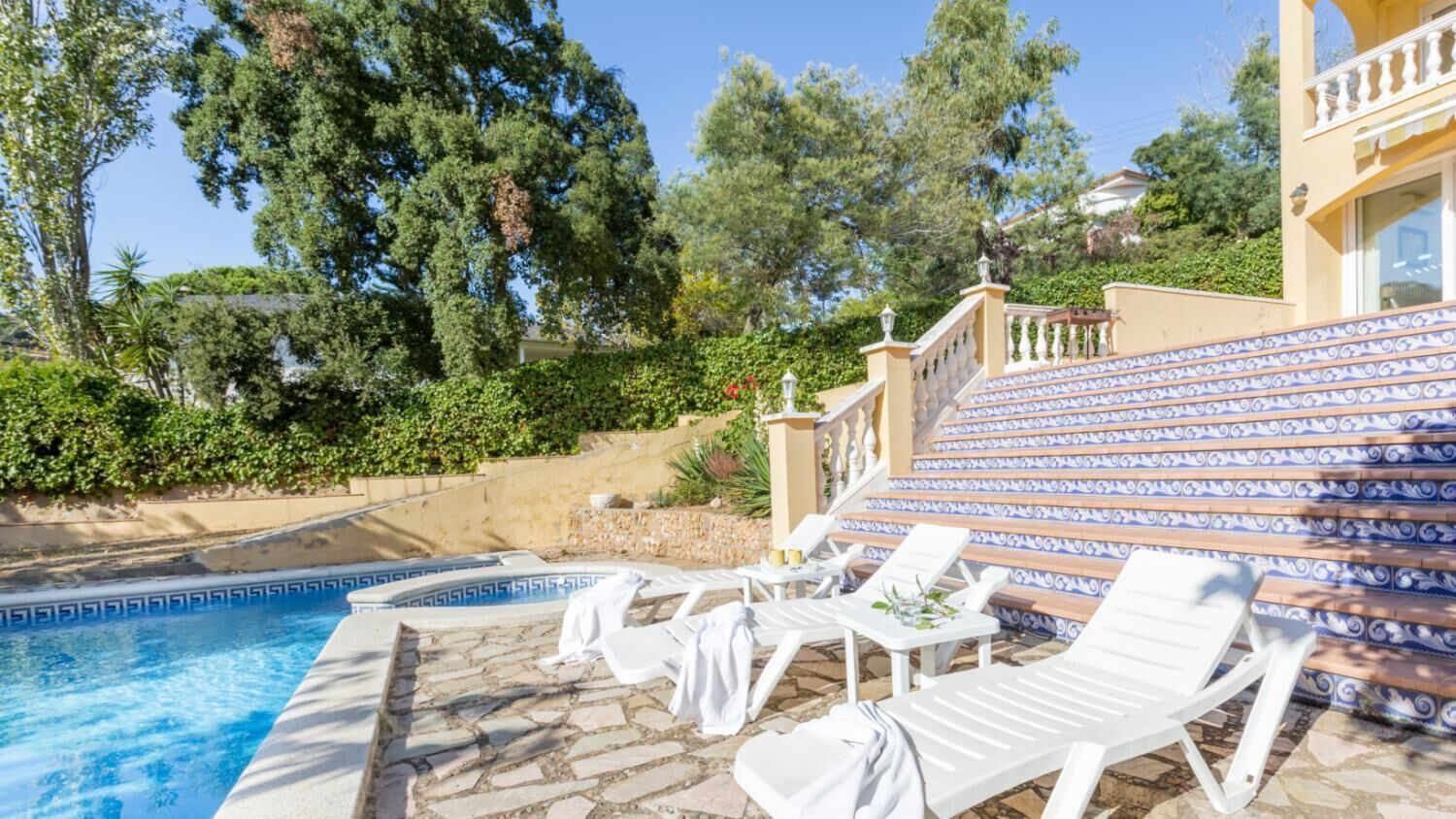 Un espace piscine avec des chaises longues et un escalier recouvert de carreaux bleus et blancs.