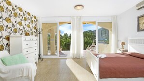 Un dormitorio con cama, cómoda, silla y vista al exterior a través de un ventanal.