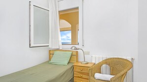 Una habitación pequeña y limpia con una cama individual, una mesita de noche, un sillón de mimbre y una ventana con vistas.