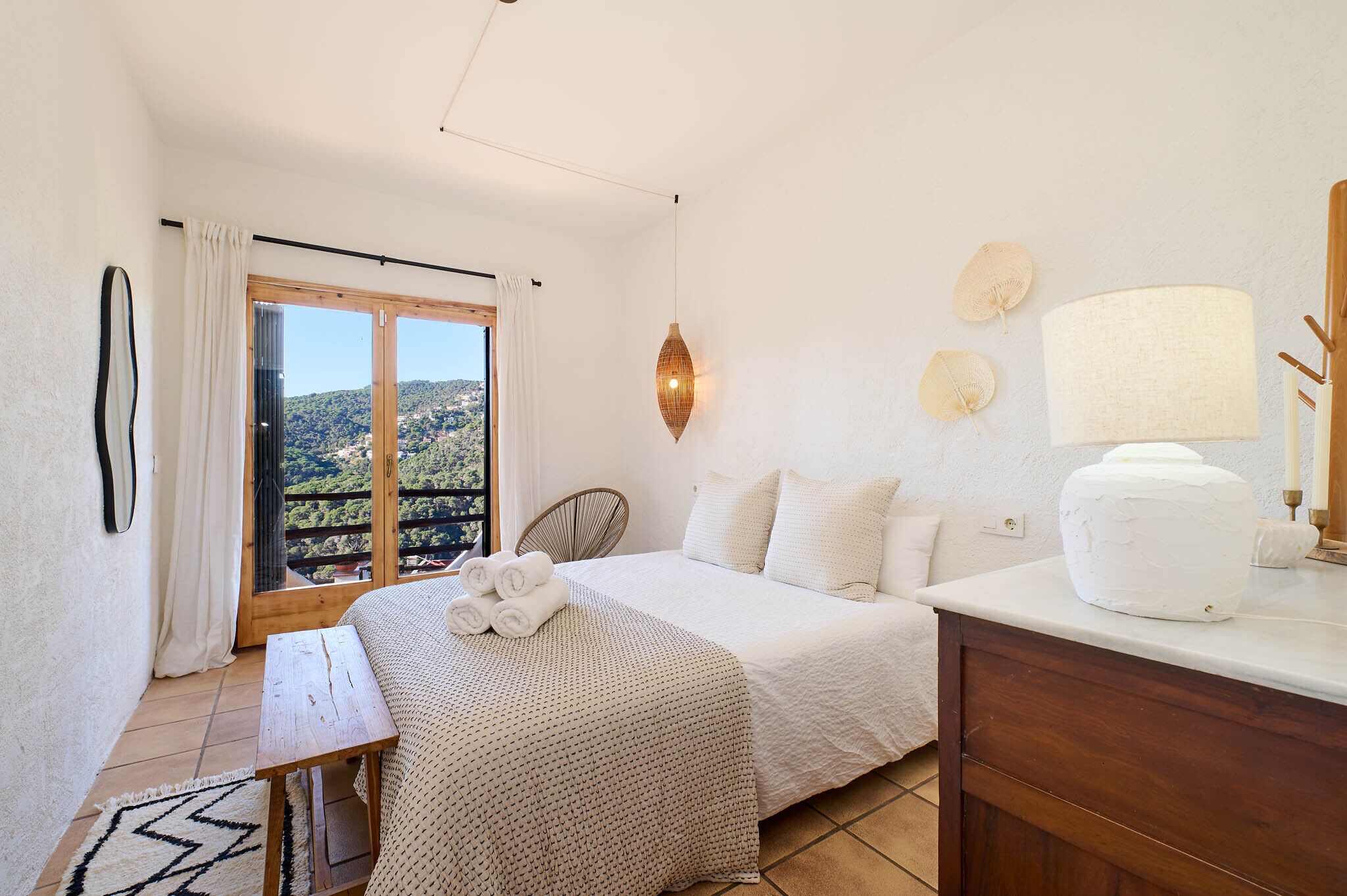 Un dormitorio con cama, mesita de noche, lámpara, una silla y vistas al exterior.