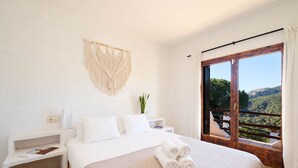 A bedroom with a bed, a nightstand, a macrame wall hanging, and a view of a forest through a sliding glass door. - Serena in Lloret de Mar (Lloret de Mar)