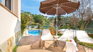 A poolside area with lounge chairs, an umbrella, and a small table with fruits. - Vila Lina in Lloret de Mar (Lloret de Mar)