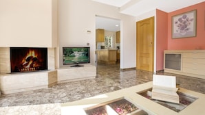 A living room with a fireplace, a flat-screen TV, a kitchen in the background, and a door leading to another room. - Vila Lina in Lloret de Mar (Lloret de Mar)